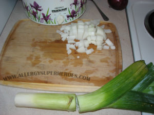 Chopped onions on wooden cutting board and a leek ready to be chopped | by Food Allergy Superheroes