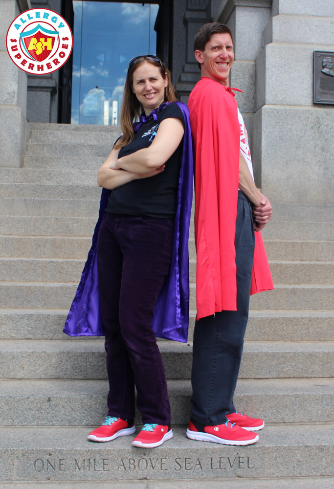 Eileen and Dean of Allergy Superheroes stand back-to-back outside the Colorado State Capitol in red sneakers, Allergy Superheroes shirts, and capes | by Food Allergy Superheroes